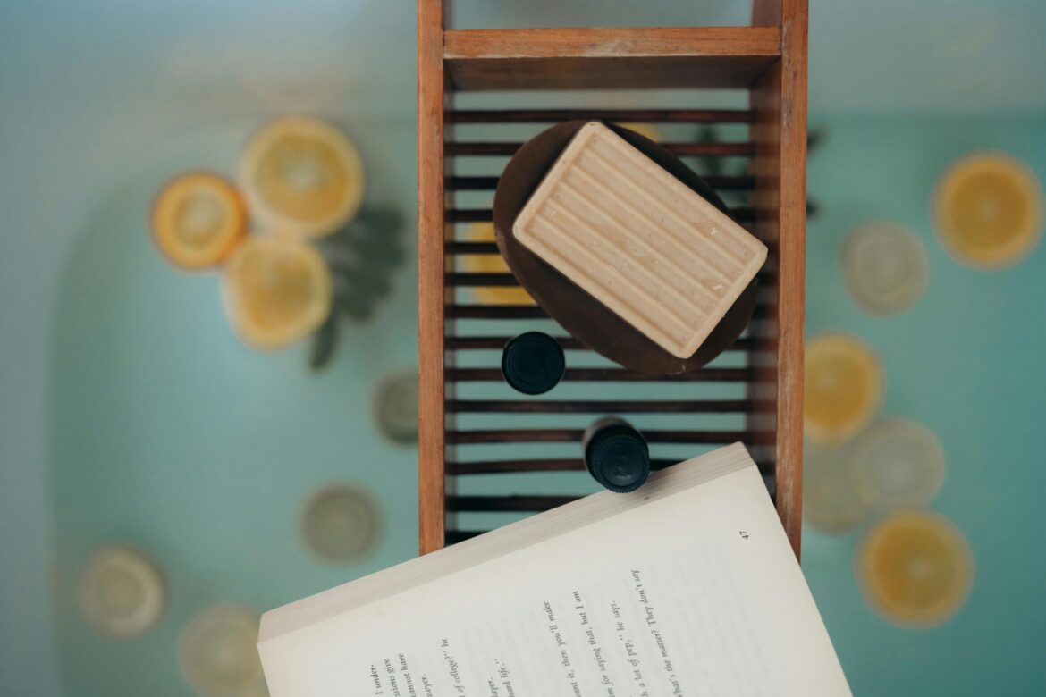 Top view of a calming bath scene with natural soap, citrus slices, and a book, ideal for relaxation.